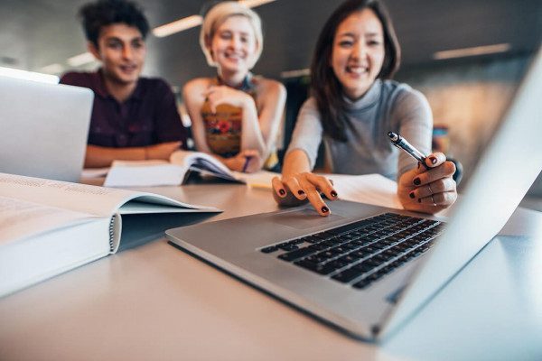 Group of happy friends working on laptop in class
