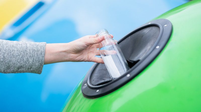Female hand throwing empty glass bottle into yellow recycle bin container outdoors, unrecognizable woman enjoying waste sorting ang garbage recycling, cropped image with selective focus, closeup