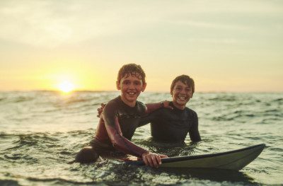Portrait of two young brothers sitting on their surfboards in the ocean.