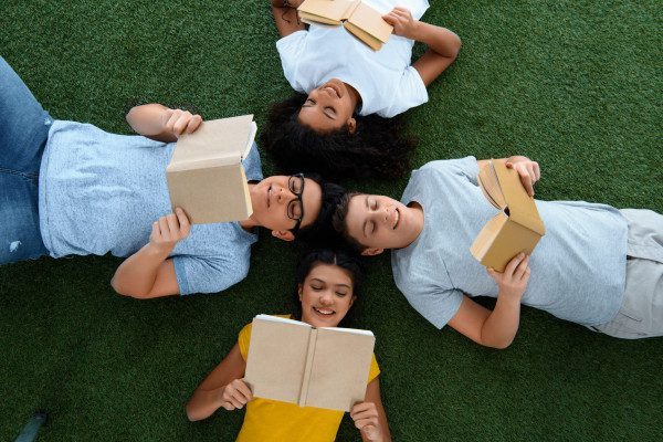top view of group of teen students reading books on green grass