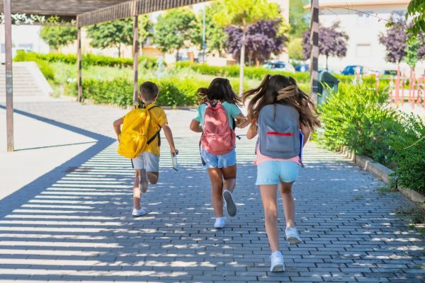 Rear View Of A Group Of Children Running With Backpacks On The First Day Of School. 3 classmates back to school. Education