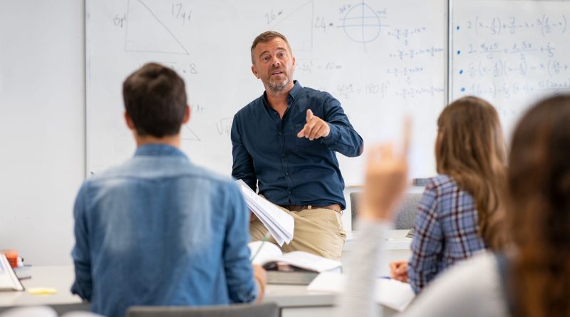 Professor pointing at college student with hand raised in classroom. Student raising a hand with a question for the teacher. Lecturer teaching in class while girl have a question to do during a math lesson.