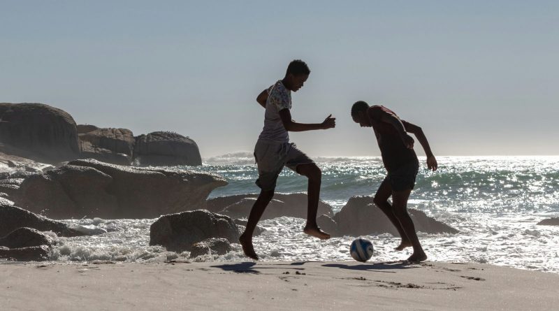 Dos hombres jugando al fútbol cerca del mar