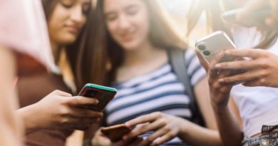 Group of teenage students standing in schoolyard and using mobile phones. They are very happy and playful.