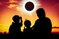 Natural phenomenon. Silhouette back view of family sitting and relaxing together. Boy point to solar eclipse on gold sky background. Happy family spending time together. Outdoor.
