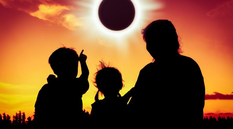 Natural phenomenon. Silhouette back view of family sitting and relaxing together. Boy point to solar eclipse on gold sky background. Happy family spending time together. Outdoor.